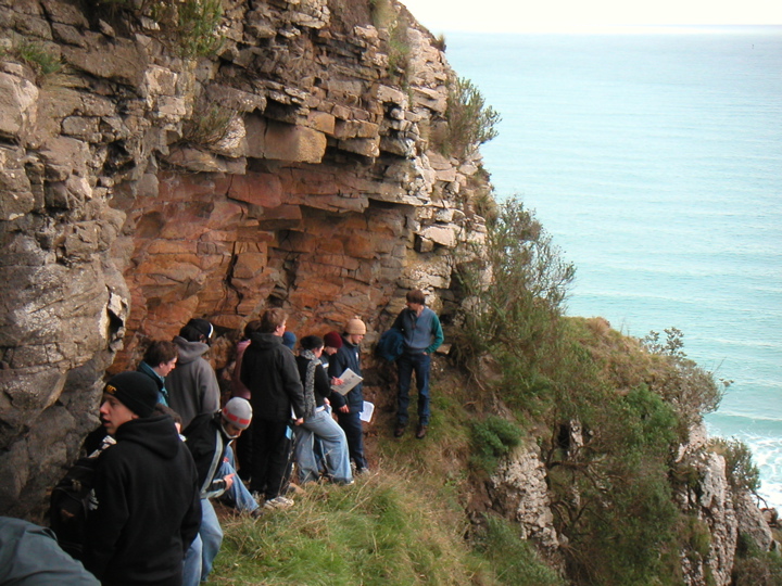 An outcrop we visited higher up the slope.  The professor is the guy at the far end musing at the lovely rocks.  They may just look like rocks to you, but actually it is amphibole basalt with unusual phenocrysts and xenoliths separated by fine-grained tuff.  Yes, this is how they "explain" stuff!  As far as I can tell, all that it means is, the rock used to be hot and liquid, and contains bits of other types of rocks and crystals.  In this case, a particular mixture of bits of rocks and crystals that is not found anywhere else in the world.